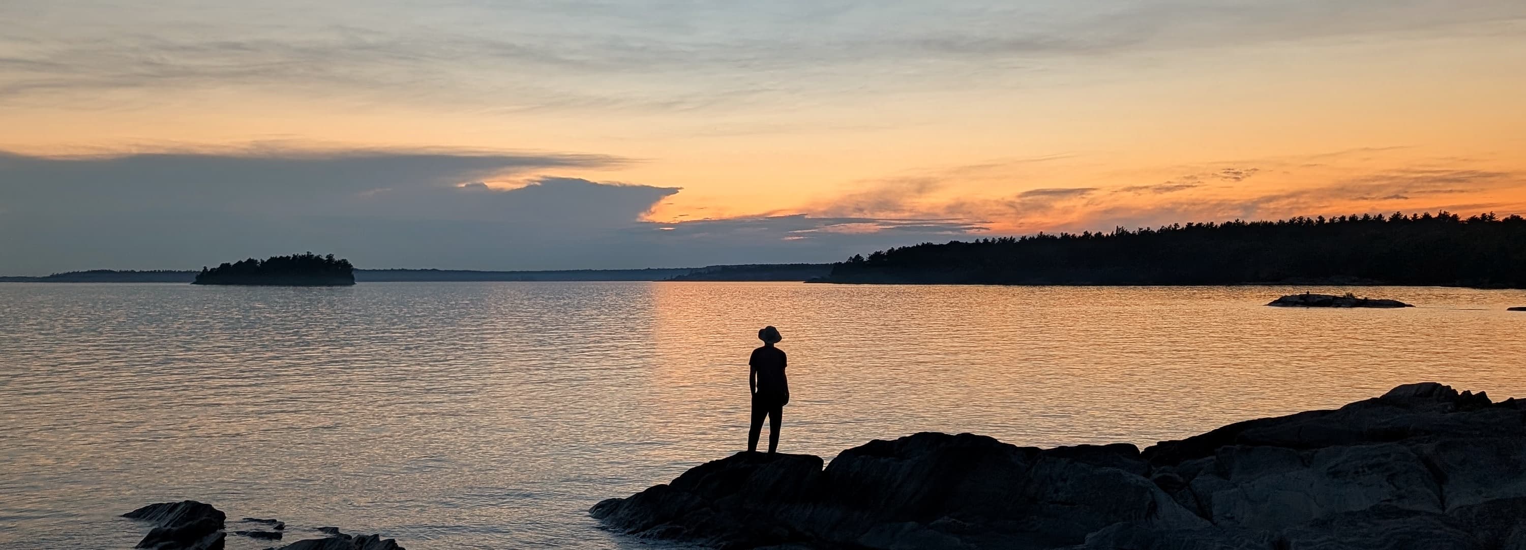 Killbear, Canada | 2025 A silhouetted voyager looks towards a deep dusk on the rocks of Georgian Bay